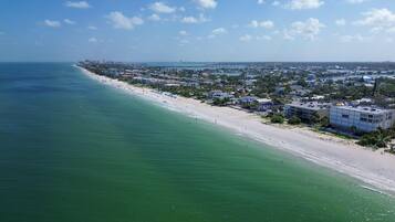 A coastal town with a long sandy beach, buildings along the shore, and a clear blue sky.