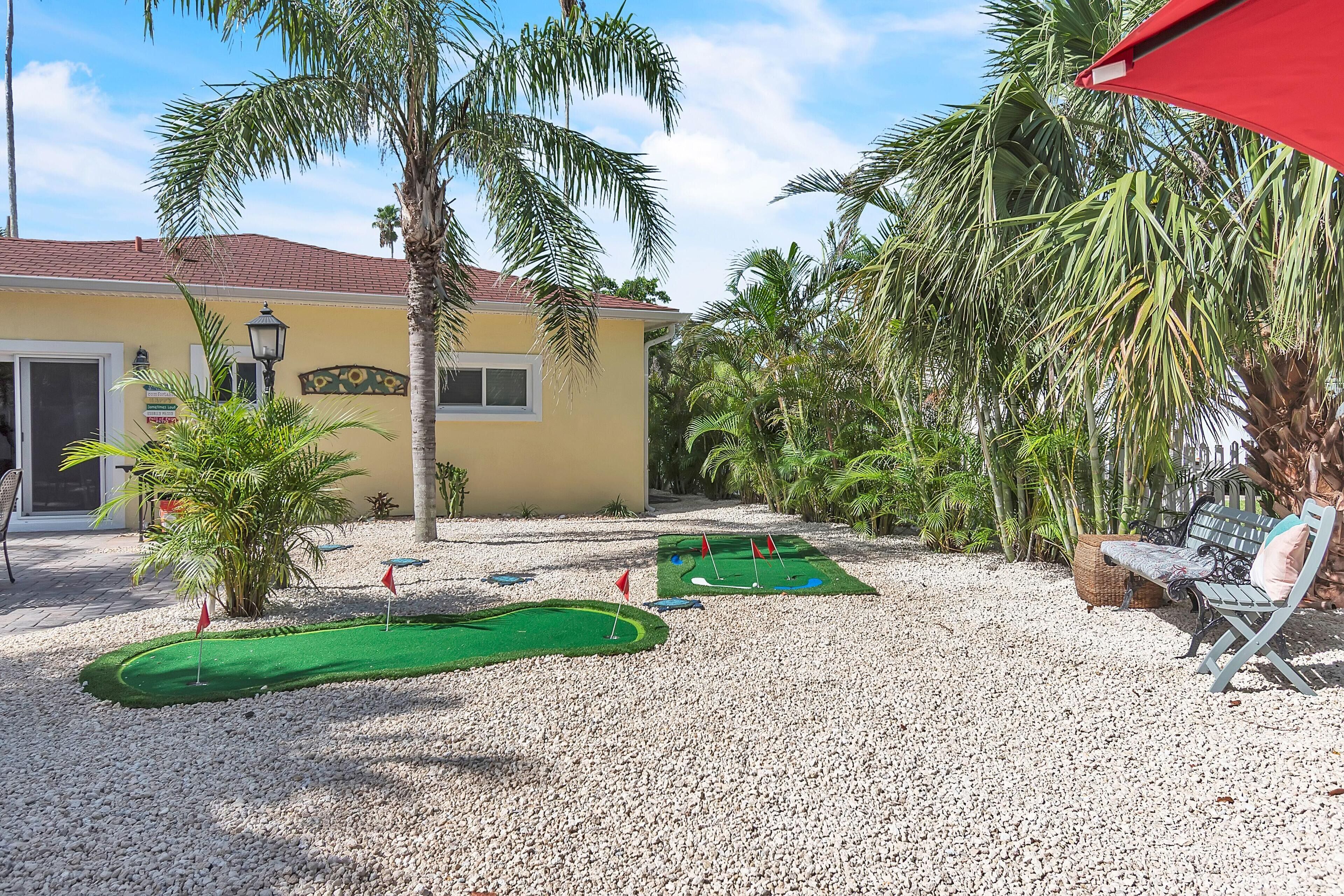 A miniature golf course with two holes, surrounded by palm trees and a bench.