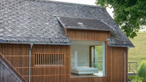 Ein modernes Haus mit schrägem Dach, Holzfassade und einer Glastür, die zu einem Schlafzimmer mit einem Bett führt.