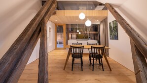 Ein Essbereich mit einem Holztisch und Stühlen, im Hintergrund eine Küche und freiliegende Holzbalken.
