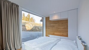 Ein modernes Schlafzimmer mit großem Fenster, Holz-Kopfteil und einem weißen Bett.