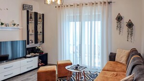 A modern living room with a sofa, ottomans, a TV, and a decorative shelf. - Villa Balani (Shiroka)