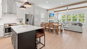 A modern kitchen with white cabinets, a central island, and a dining area with wooden chairs and a table. - 6 Ensuite Bedrooms, Pool, Close to Beach, Luxury (Santa Rosa Beach)