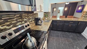 Une cuisine moderne avec un cuisinière en acier inoxydable, des armoires noires et un sol en marbre.