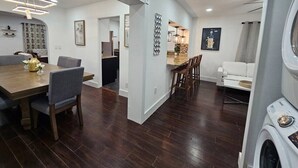 Une cuisine moderne avec un plancher en bois foncé, un coin repas avec une table et des chaises en bois, et un salon avec un canapé blanc et une table basse.