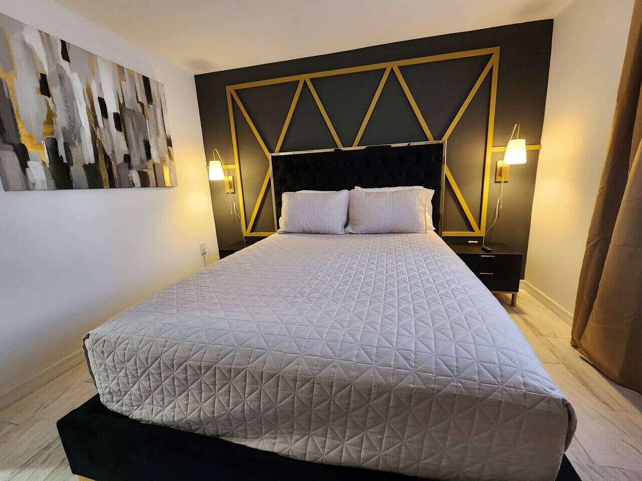 A large bed with a quilted headboard, bedside lamps, and a geometric wall design.