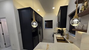 A modern kitchen with black cabinets, a white marble countertop, and pendant lighting. - Triplex Sleeps17 CollegePark Golf 5min to Downtown (Orlando)
