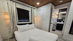 A hotel room with a large bed, a window with blinds, a bathroom with a mirror and sink, and a wooden ceiling. - Triplex Sleeps17 CollegePark Golf 5min to Downtown (Orlando)