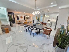 Un vaste espace de vie comprenant une grande table à manger, des sièges confortables et une cuisine moderne en arrière-plan.