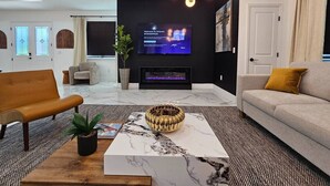 A modern living room with a flat-screen TV, a fireplace, and a sofa.