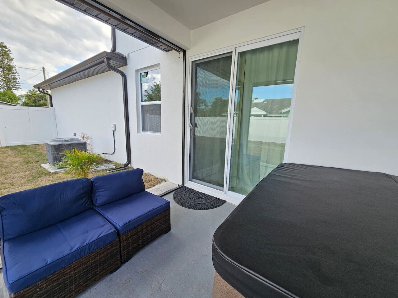A modern outdoor living area with a blue sofa, a black mattress, and a sliding glass door leading to a covered patio.