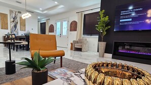 A modern living room with a fireplace, a television displaying a welcome message, and a seating area with a unique gold-colored circular coffee table.