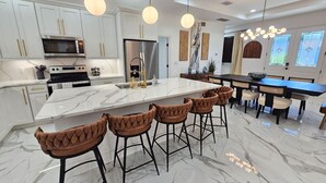 A modern kitchen with white cabinets, a large island with bar stools, and pendant lighting.
