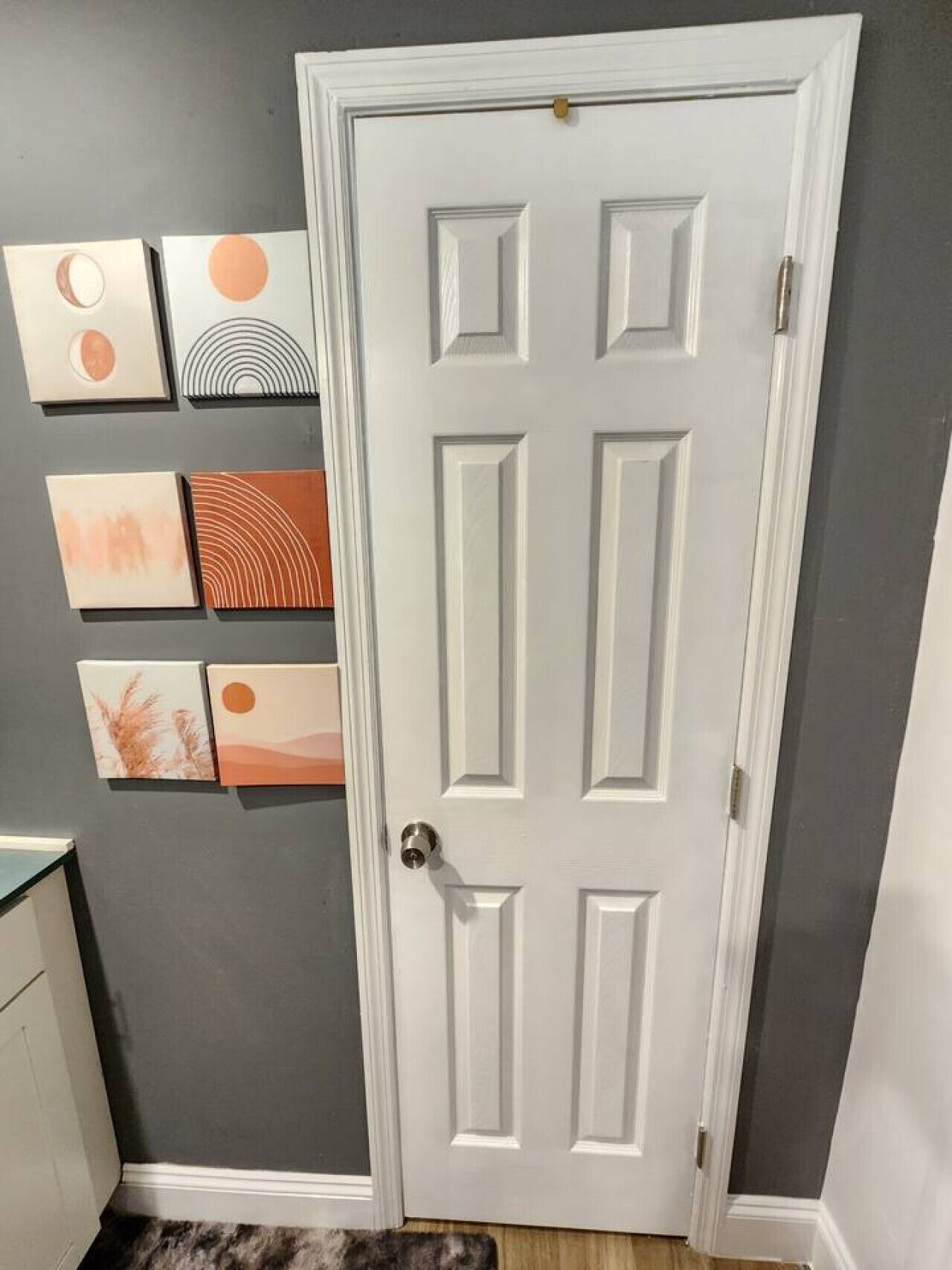 A hallway with a white door, grey walls, and artwork on the wall.