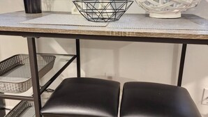 Una cocina con una mesa, dos taburetes negros, un farol decorativo blanco y una planta en maceta.