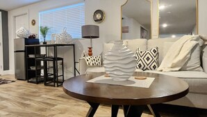 Una sala de estar moderna con una mesa de centro redonda de madera, un sofá con cojines estampados y un comedor con una mesa y sillas de metal negro.