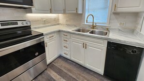 A modern kitchen with white cabinetry, stainless steel appliances, and a window with blinds.
