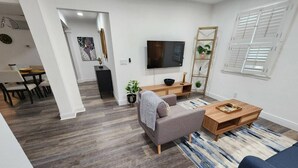 A modern living room with a grey sofa, a wooden coffee table, and a TV mounted on the wall.