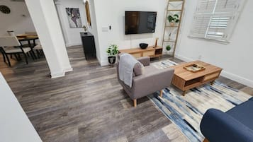 A modern living room with a grey sofa, a wooden coffee table, and a TV mounted on the wall.