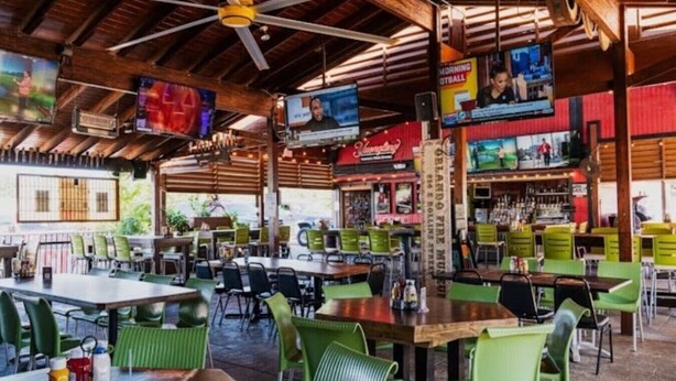 A restaurant with wooden ceiling beams, green chairs, and multiple TVs on the walls.