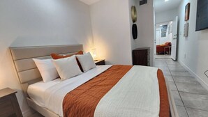 Un dormitorio moderno con una cama grande, una mesita de noche, una lámpara y vistas a otra habitación.