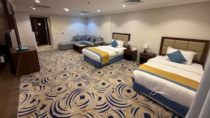 A hotel room with two beds, a sofa, a desk, and a patterned carpet.