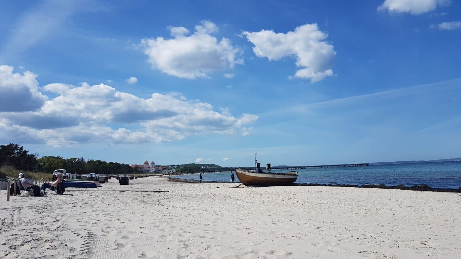 Een zandstrand met een boot, een pier en een gebouw in de verte.