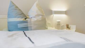 Ein ordentlich bezogenes Bett mit Kissen, ein Nachttisch mit Lampe und ein kleiner Stuhl.