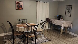A dining area with a round table, four chairs, a coffee machine, and a refrigerator.