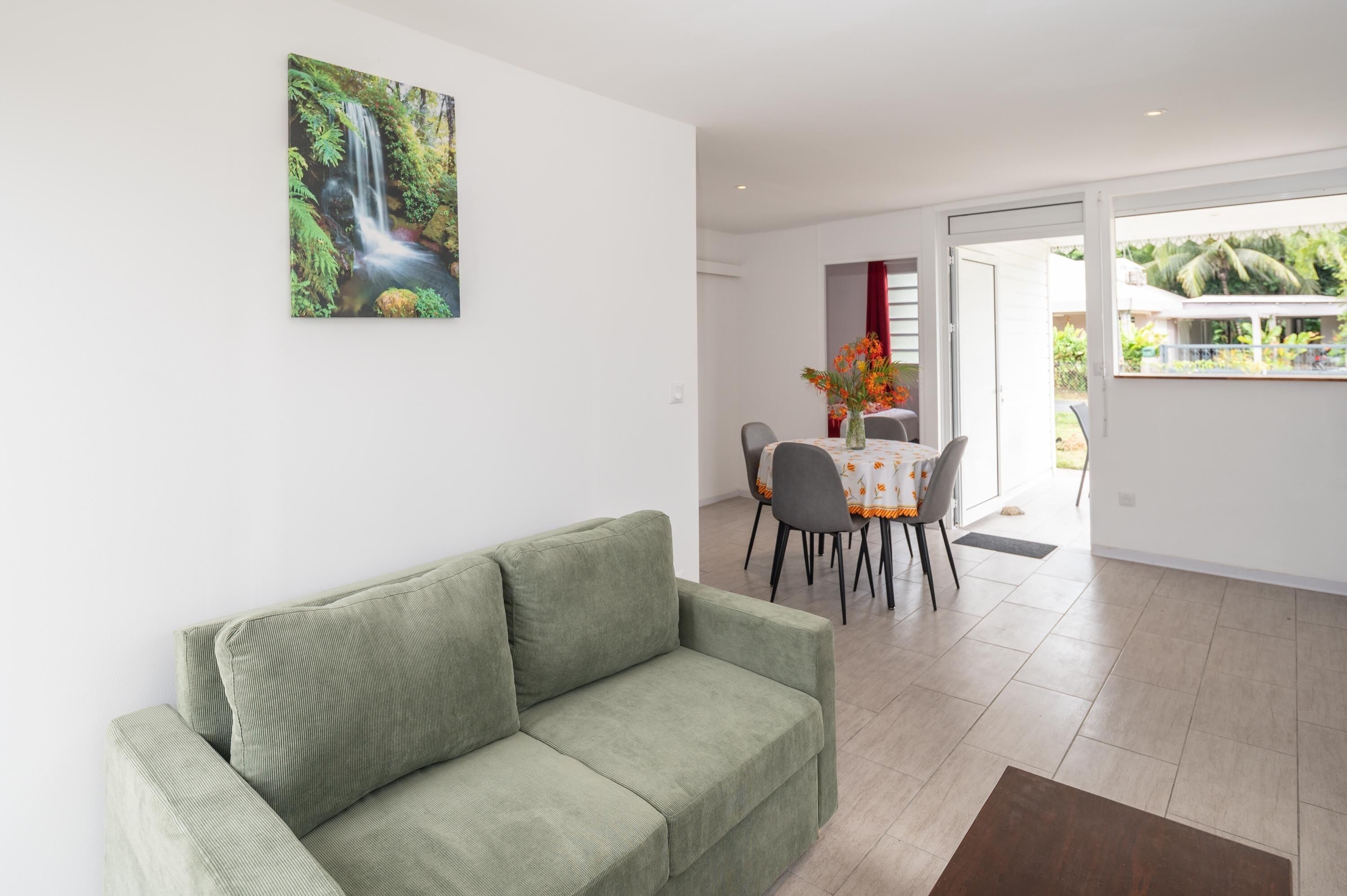 En stue med en grøn sofa, et spisebord med stole, og et maleri af et vandfald.