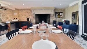 Un comedor con una larga mesa de madera dispuesta para seis personas, rodeada de sillas, y una pared de piedra y chimenea al fondo.