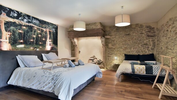 Un dormitorio con una cama grande, una cama más pequeña, un banco de madera y una pared de piedra.