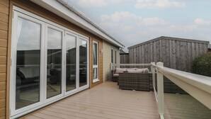 A covered deck with sliding glass doors, a wooden fence, and outdoor furniture. - Platinum Lodge (Talybont)