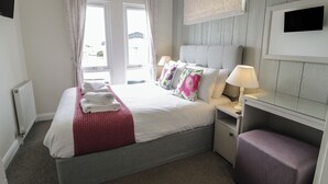 A neatly arranged bedroom with a bed, bedside tables, a lamp, and a window with curtains. - Platinum Lodge (Talybont)