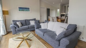 A living room with two grey sofas, a glass coffee table, and a patterned rug. - Platinum Lodge (Talybont)