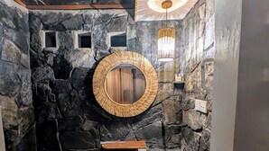 A bathroom with a stone wall, a round mirror, a sink, and a toilet. - Nomads Hideaway Near Matara Railway Stat (Matara)