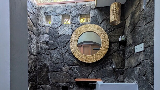 A bathroom with a stone wall, a round mirror, a sink, and a toilet. - Nomads Hideaway Near Matara Railway Stat (Matara)