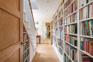 Een gang met houten boekenkasten vol boeken, die leidt naar een kamer met een bureau en stoel.