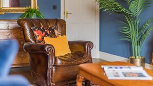 A brown leather armchair with a yellow cushion, a wooden side table with papers, a large potted plant, and a mirror on the wall. - Harbour Master, Whitstable, Kent (Whitstable)