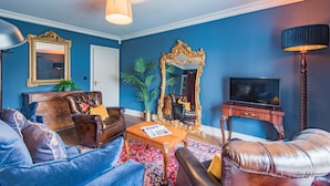 A living room with blue walls, a large mirror, leather sofas, a wooden coffee table, and a television. - Harbour Master, Whitstable, Kent (Whitstable)