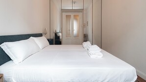 A neatly made bed with white linens, a dark headboard, and a row of folded towels on the foot of the bed.
