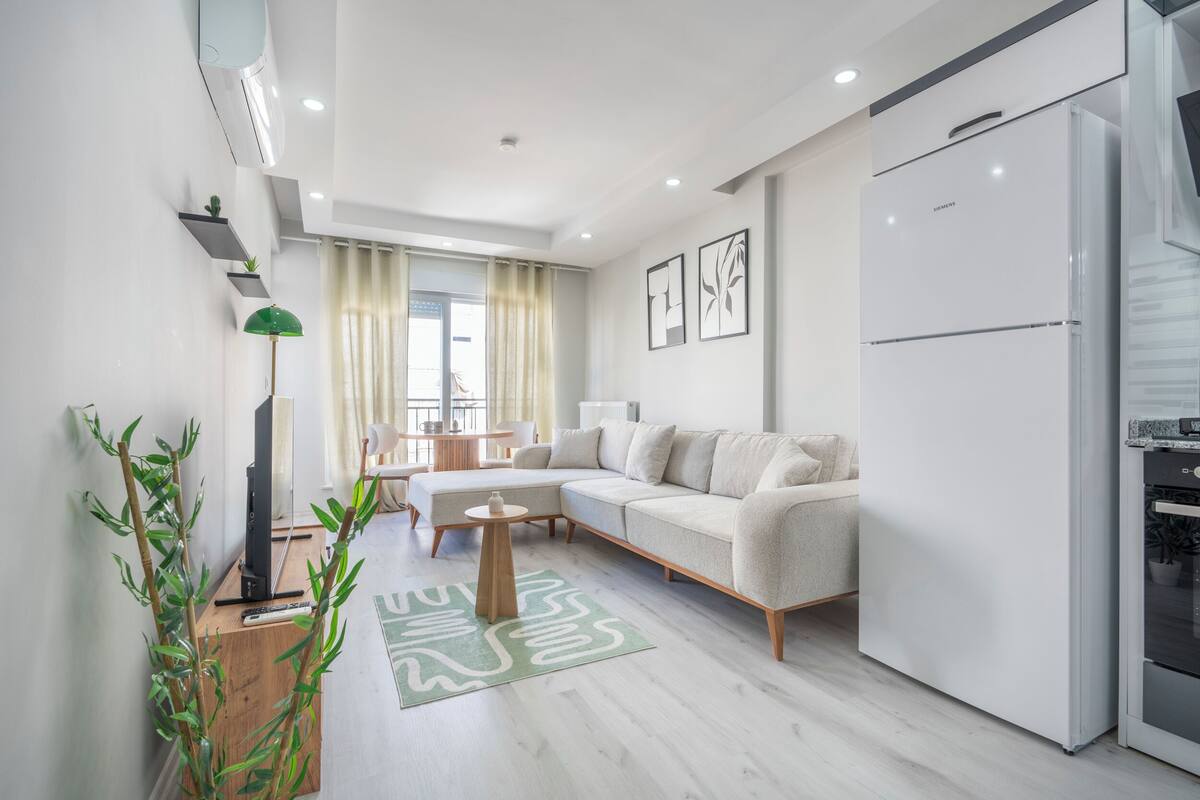 A modern living room with a sofa, a coffee table, a TV, and a kitchen area with a refrigerator.