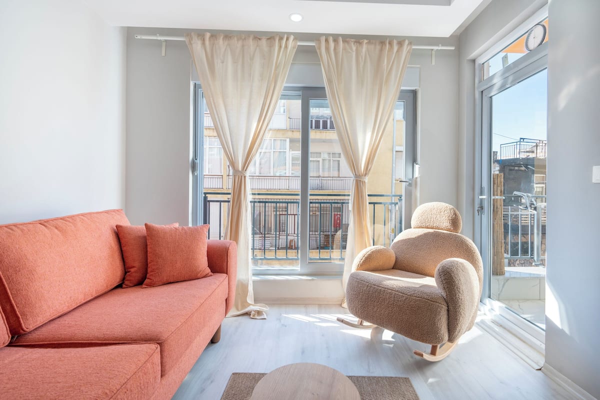 A modern living room with a sofa, a chair, and a large window with curtains.