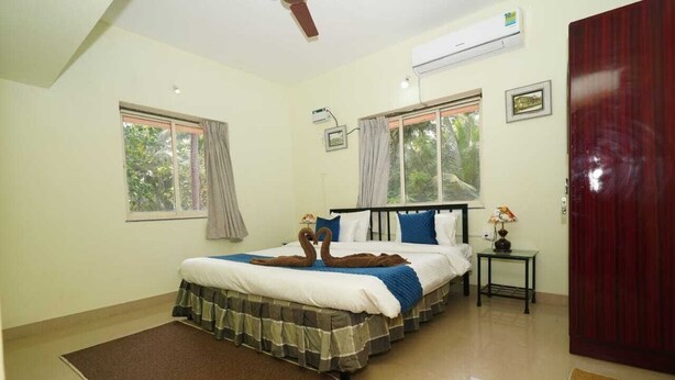 A bedroom with a bed, two windows, an air conditioning unit, a small table, and a door. - Four Seasons GuestHouse (Utorda)