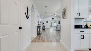 A spacious hallway with a wooden floor, white walls, and a kitchen area with white cabinets and a black countertop. - The Dive Locker- 5 min to the Beach Sleeps 10 (Panama City Beach)