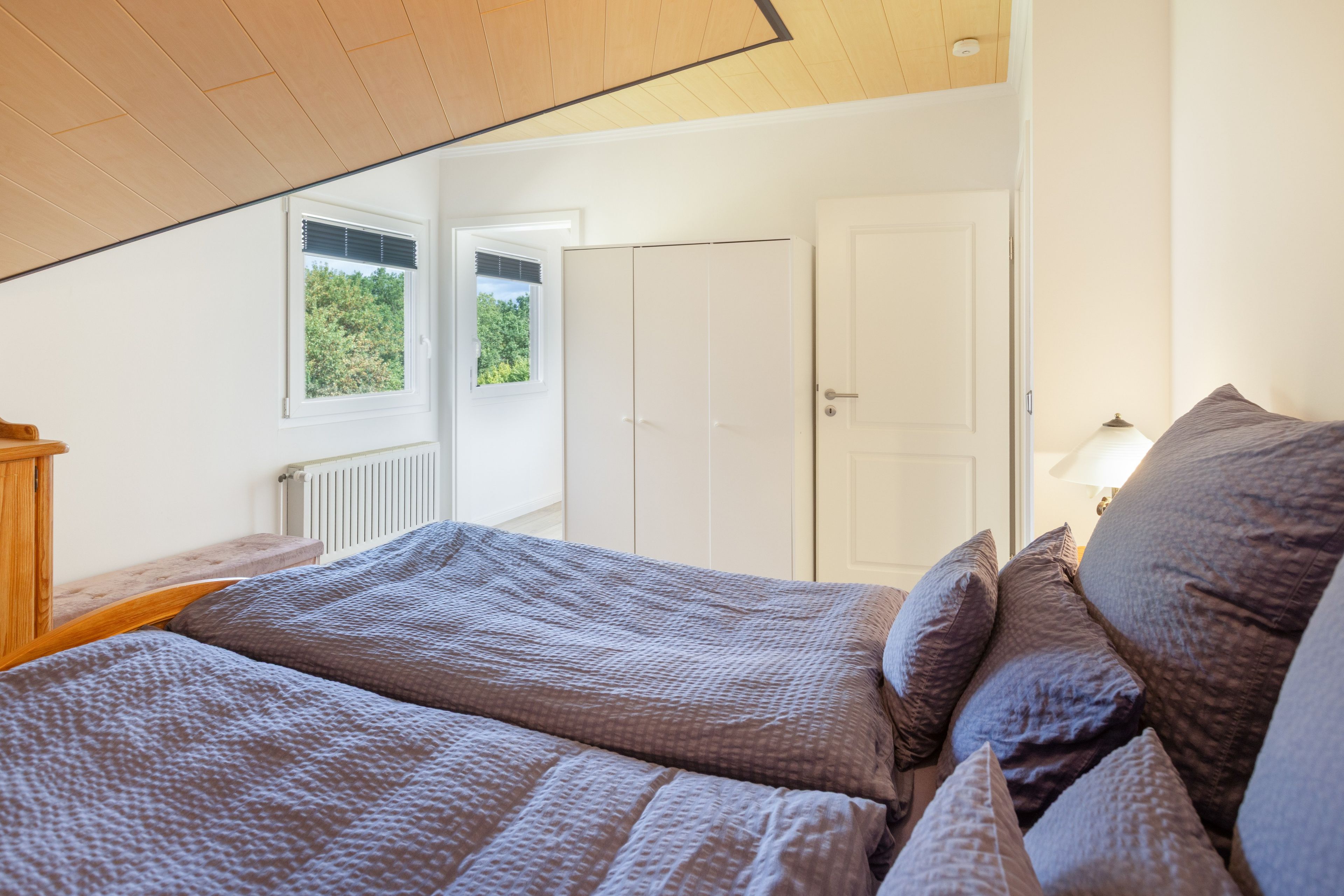 A bedroom with a sloped ceiling, a bed with a patterned duvet, a bedside table, and a window with blinds.