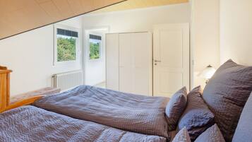 A bedroom with a sloped ceiling, a bed with a patterned duvet, a bedside table, and a window with blinds.