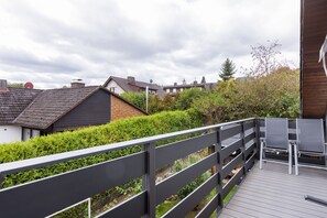 A wooden deck with a metal railing, overlooking a residential area with houses and a hedge.