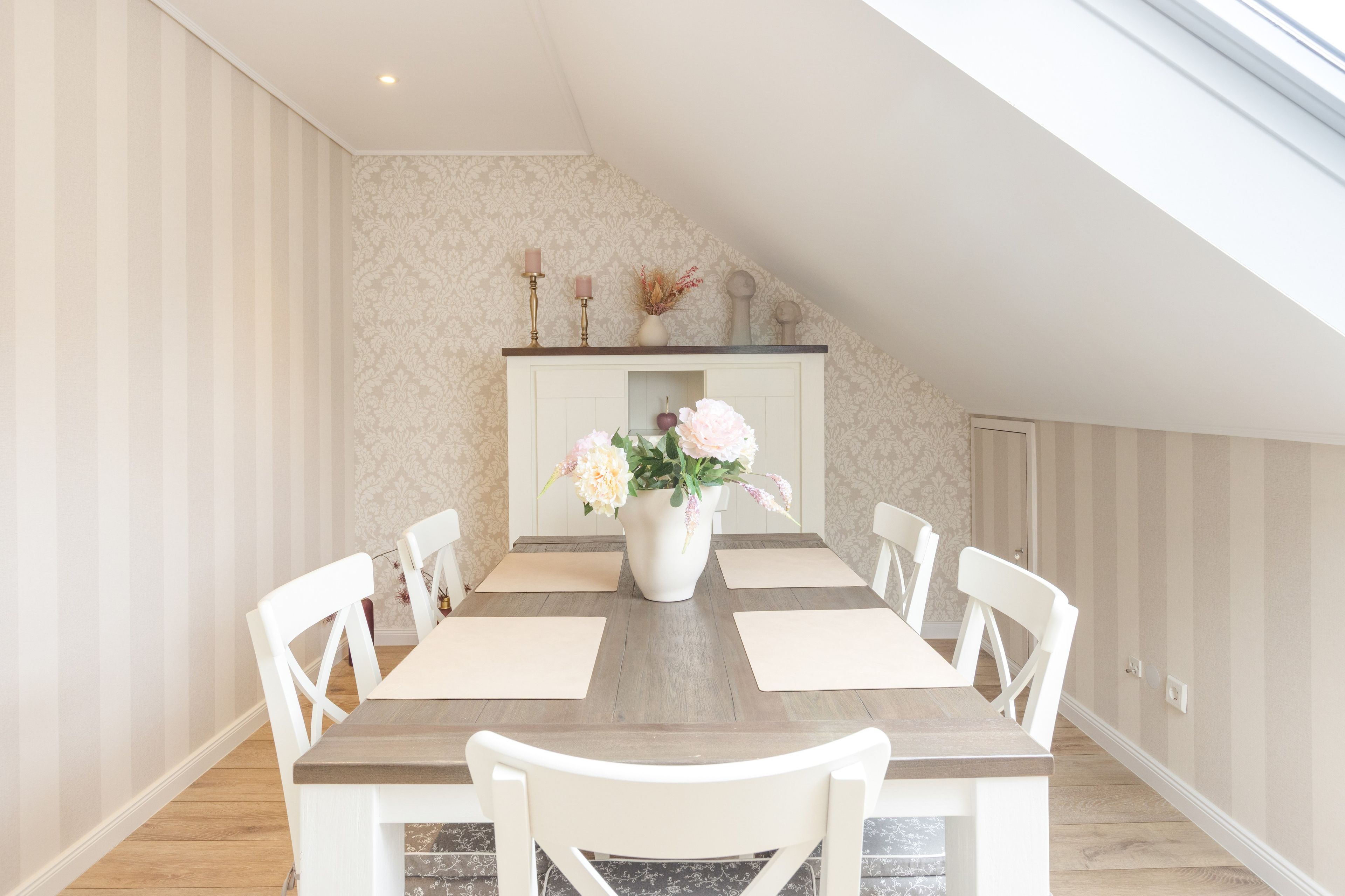 Un coin repas avec une table en bois, des chaises blanches, un vase de fleurs et une cheminée décorative.
