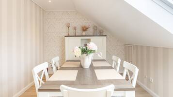 Un coin repas avec une table en bois, des chaises blanches, un vase de fleurs et une cheminée décorative.